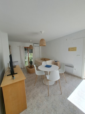 Ein modernes Zimmer mit Esstisch, Stühlen, Fernseher und Fenster.