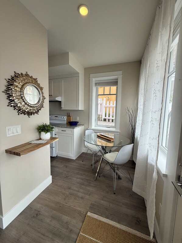 A compact kitchen with white cabinets, a built-in oven, and a dining area with a glass table and white chairs.