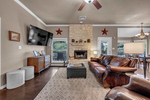 A living room with a stone fireplace, leather sofa, and a flat-screen TV. - Pop's Place: Private Pool & Lake Access! (Granite Shoals)
