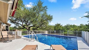 Piscina com um deck, espreguiçadeiras e uma árvore ao fundo.