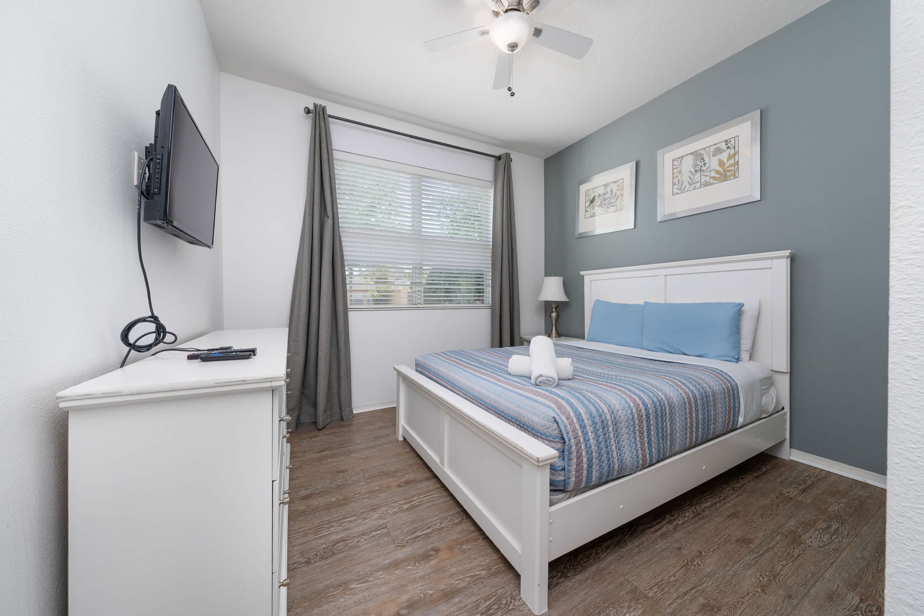 A bedroom with a bed, a desk, a ceiling fan, and a window with curtains.