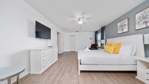 Quarto com uma cama, televisão, ventilador de teto e cômoda branca.