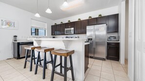 Cozinha moderna com ilha central, banquetas, eletrodomésticos de aço inoxidável e iluminação pendente.