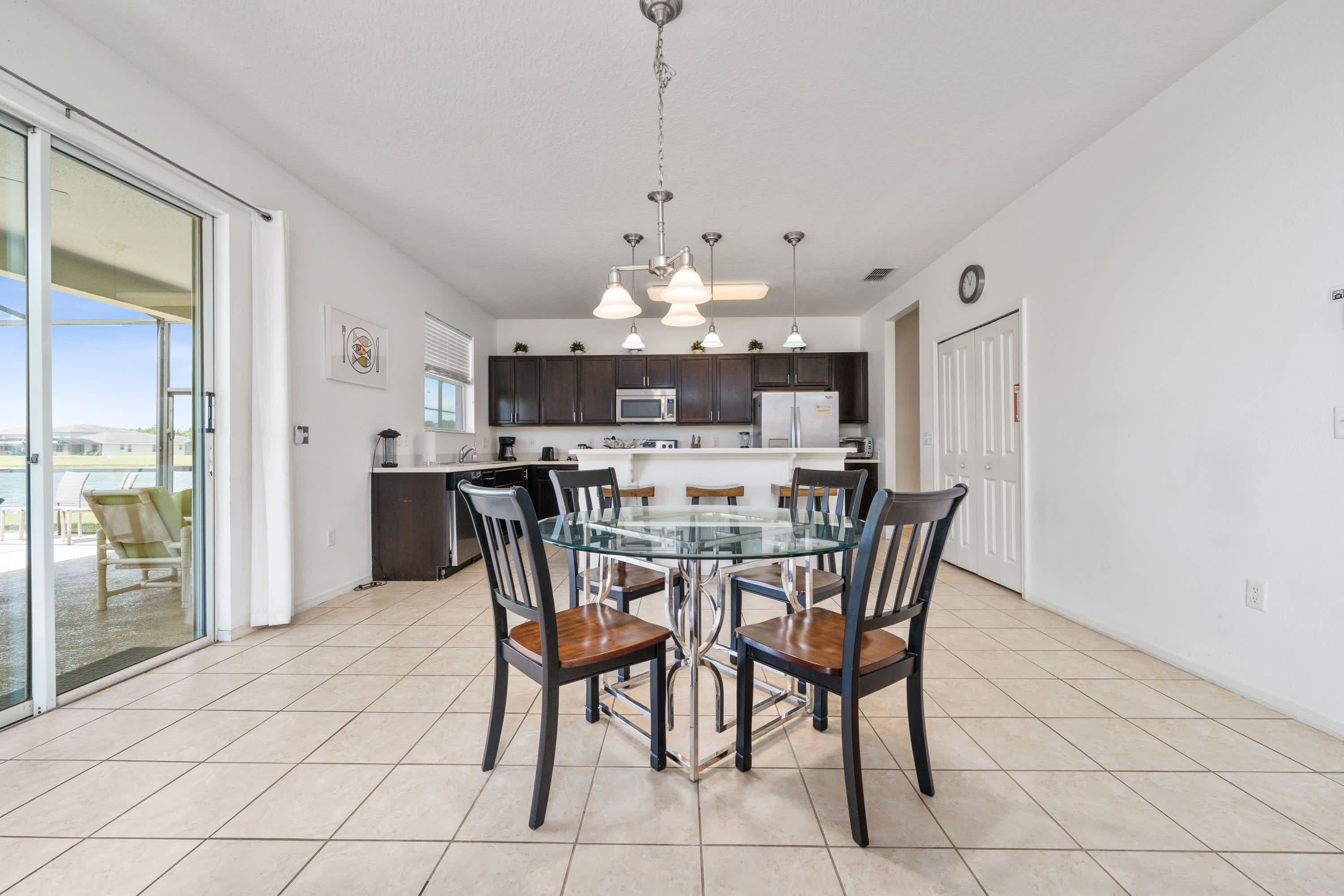 A modern kitchen with dark cabinets, a glass dining table, and pendant lighting.