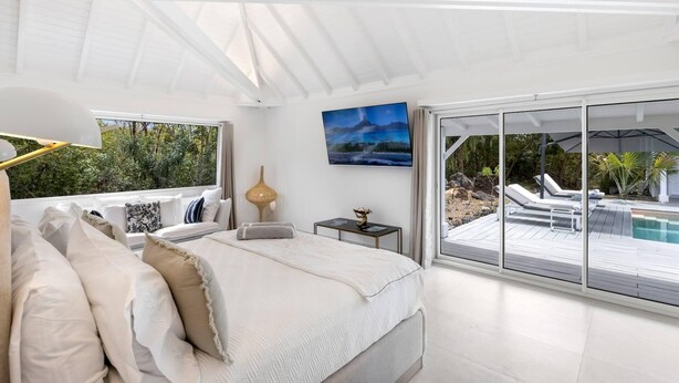 Een moderne slaapkamer met een groot bed, een televisie en uitzicht op een zwembad en terras.