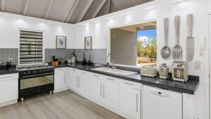 Een moderne keuken met witte kasten, een zwart aanrecht, een gasfornuis, een vaatwasser en een raam met uitzicht op de omgeving.