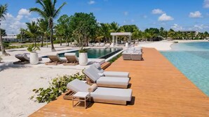 Une terrasse en bois avec des chaises longues, une piscine et une plage.