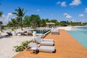 Um deck de madeira com espreguiçadeiras, uma piscina e uma praia.