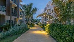 Un chemin bordé de bâtiments modernes dotés de balcons, de palmiers et d’une végétation luxuriante et bien entretenue.