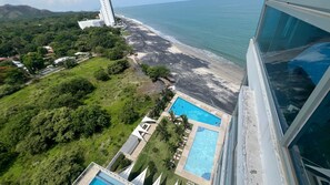 An aerial view of a coastal area with a beach, a swimming pool, and a building with a balcony overlooking the sea. - Stunning mountain ocean view 2 beds 2 baths Gorgona (Nueva Gorgona)