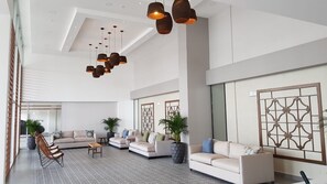 Un hall d’entrée spacieux avec un plafond haut, des luminaires modernes et un espace détente avec des canapés et des fauteuils.