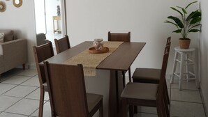 A dining area with a wooden table, six chairs, a painting of beach huts, a potted plant, and a white air conditioning unit on the wall. - Central Zone Department (La Paz)