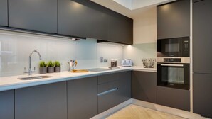 A modern kitchen with dark cabinetry, a stainless steel sink, a microwave, and an oven. - Apex Executive Apartments - The Benson (Dublin)
