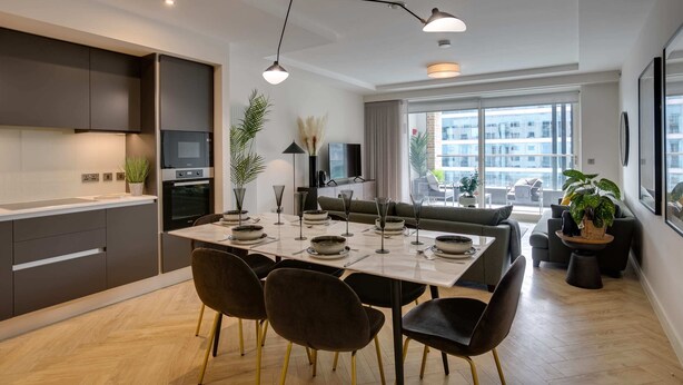 A modern kitchen with dark cabinets, a dining table set for four, and a large window with a city view. - Apex Executive Apartments - The Benson (Dublin)