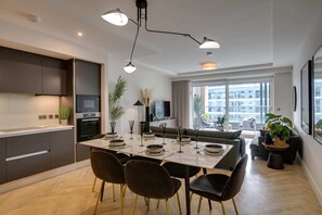 Eine moderne Küche mit dunklen Schränken, einem Esstisch für vier Personen und einem großen Fenster mit Blick auf die Stadt.