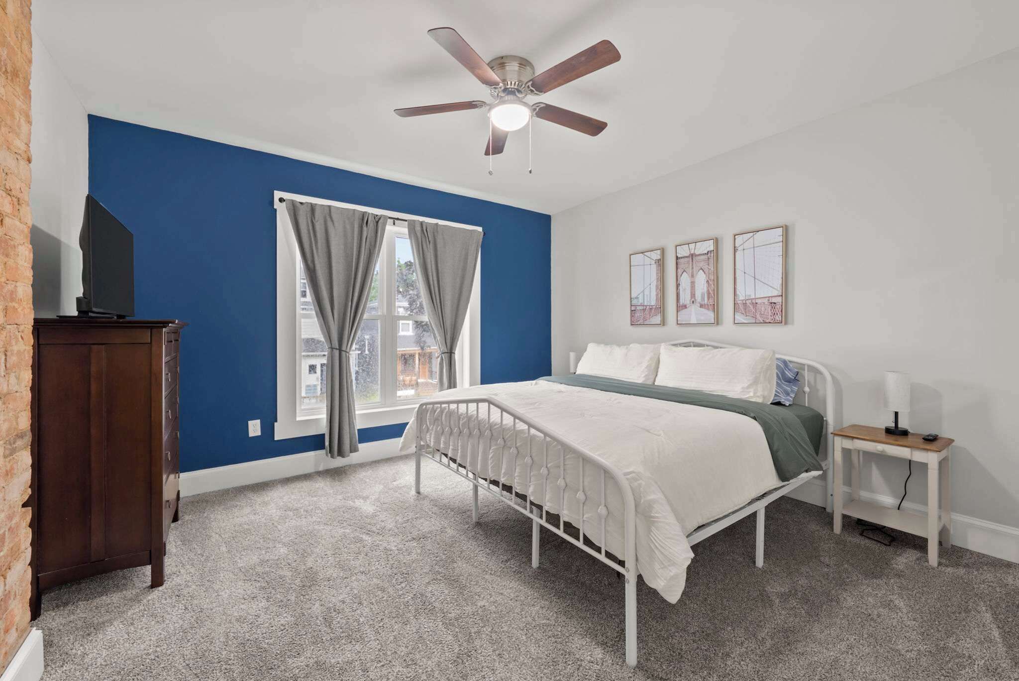 A bedroom with a bed, a nightstand, a ceiling fan, and a window with curtains.