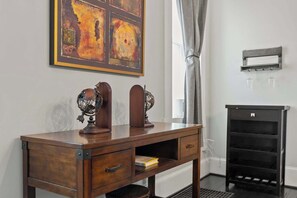 Una scrivania in legno con due lampade a sfera, una libreria e un termosifone in una stanza con una finestra e un quadro appeso al muro.