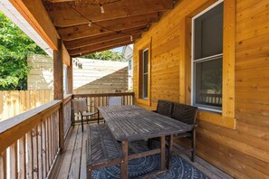 Un terrazzo in legno con tavolo e sedie, una finestra e vista su una casa sullo sfondo.