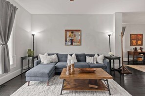 Ein modernes Wohnzimmer mit einem Ecksofa, einem Holztisch und zwei Stehlampen.