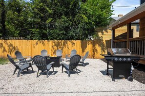 An outdoor patio with a grill, chairs, and a wooden fence. - Modern 3BR Home - FirePit + Grill - Sleeps 9 (Columbus)