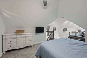 Ein Schlafzimmer mit Bett, Kommode und Blick auf einen Dachboden.