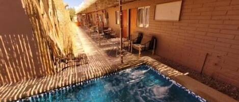 A swimming pool with clear water, surrounded by a brick wall and a thatched roof structure.