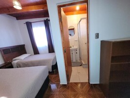 Habitación de hotel con dos camas, baño con ducha y techo de madera.