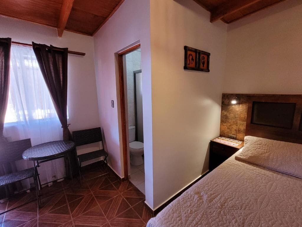 Une chambre à coucher avec un lit, une petite table, une chaise, un téléviseur et une porte menant à la salle de bain.