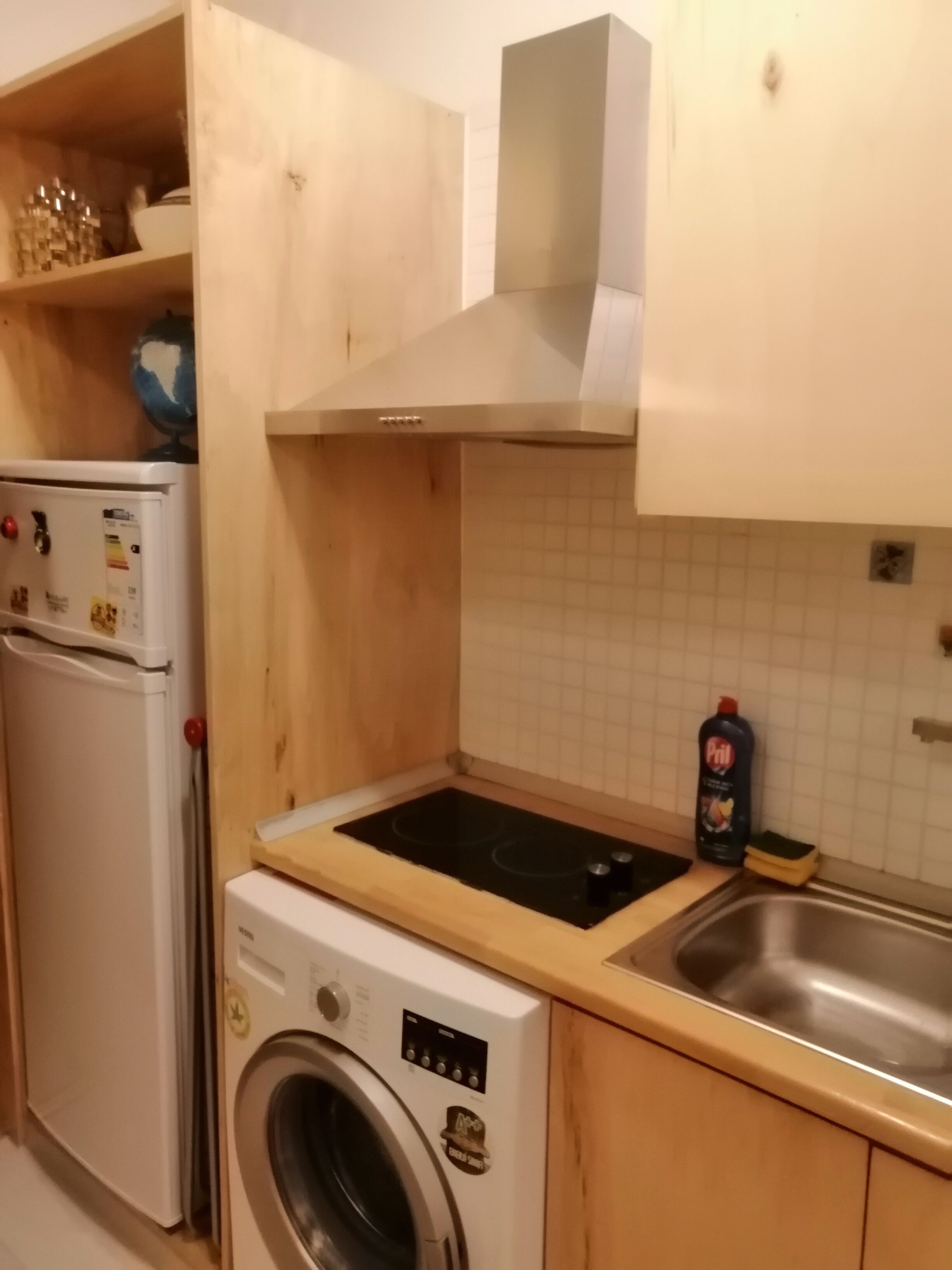 Una cucina compatta con lavatrice, un piccolo frigorifero e un lavello.