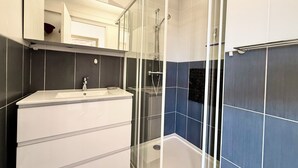 Ein modernes Badezimmer mit einer gläsernen Duschkabine, einem weißen Waschtisch mit Spiegel und blautonierten Fliesen.