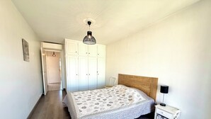 Ein Schlafzimmer mit einem hölzernen Kopfteil, einer gemusterten Bettdecke, einem Nachttisch mit einer Lampe und einem Kleiderschrank.