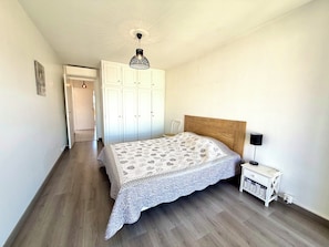 Ein Schlafzimmer mit einem hölzernen Kopfteil, einer gemusterten Bettdecke, einem Nachttisch mit einer Lampe und einem Kleiderschrank.