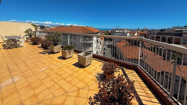Eine Dachterrasse mit Fliesenboden, Kübelpflanzen und Blick auf die Stadt und das Meer.