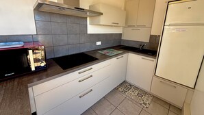 Eine moderne Küche mit weißen Schränken, einer Edelstahl-Dunstabzugshaube, einem schwarzen Induktionskochfeld und einem weißen Kühlschrank.