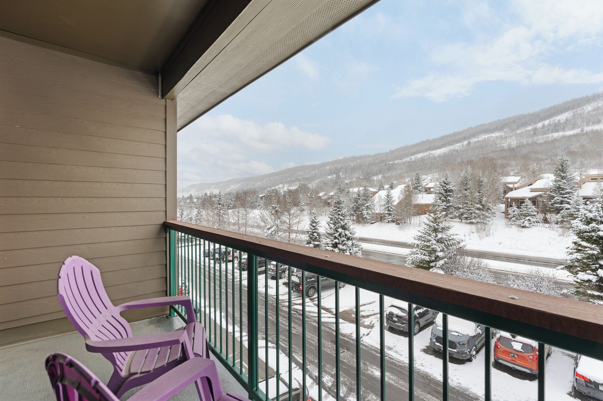 Un balcon donnant sur un paysage enneigé et des voitures garées.