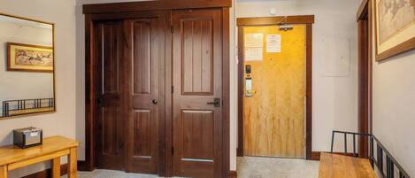 A hallway with double wooden doors, a wooden bench, a small table with a radio, and a light fixture on the ceiling.