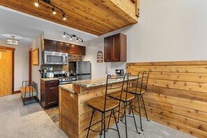 A kitchen with wooden cabinetry, a granite countertop, a stainless steel microwave, a stove, and bar stools.
