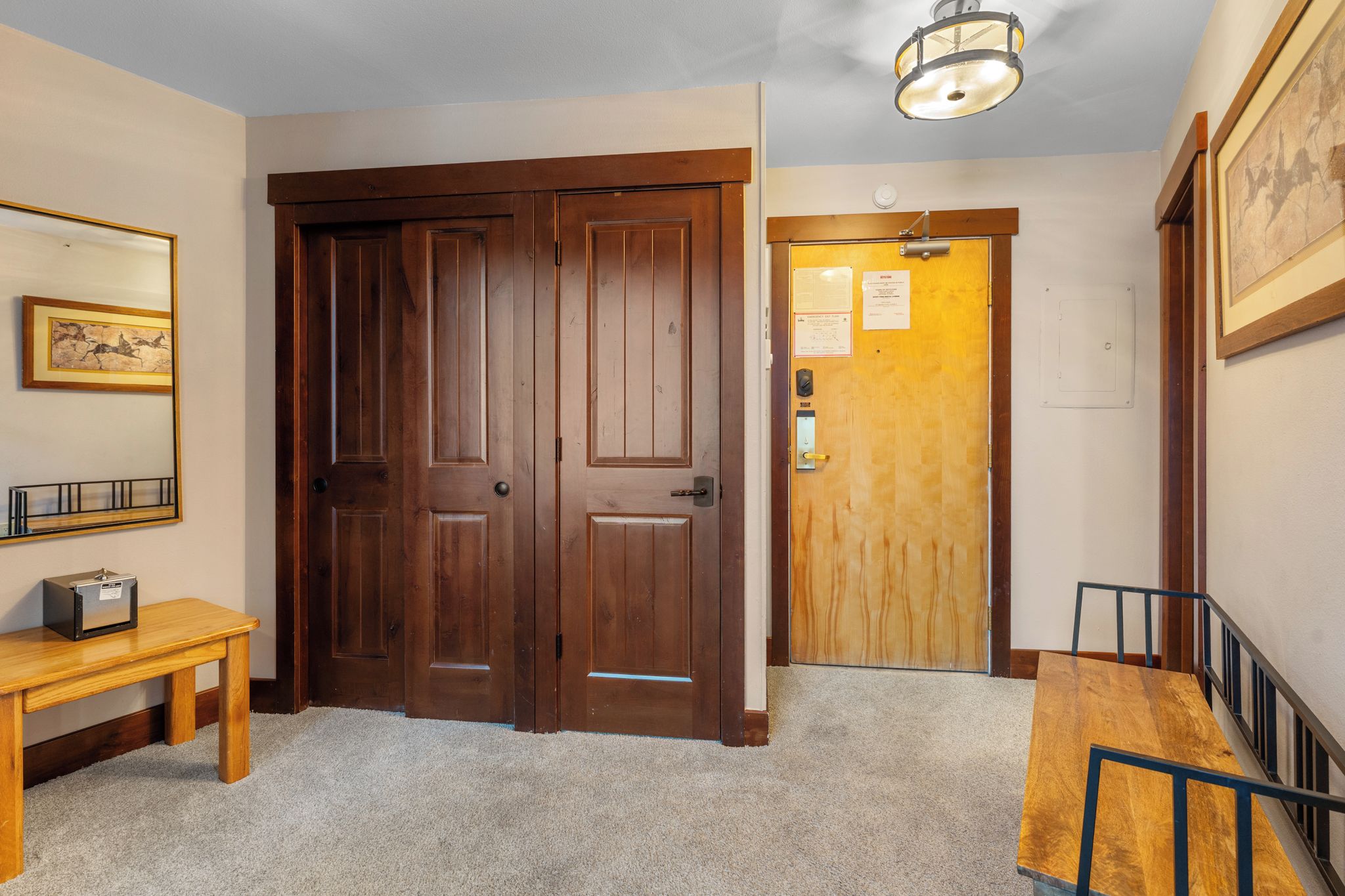 A hallway with double wooden doors, a wooden bench, a small table with a radio, and a light fixture on the ceiling.