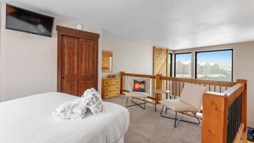 Ein Hotelzimmer mit Bett, Fernseher, Holztür, Kommode, Stuhl und einem Balkon mit Aussicht.