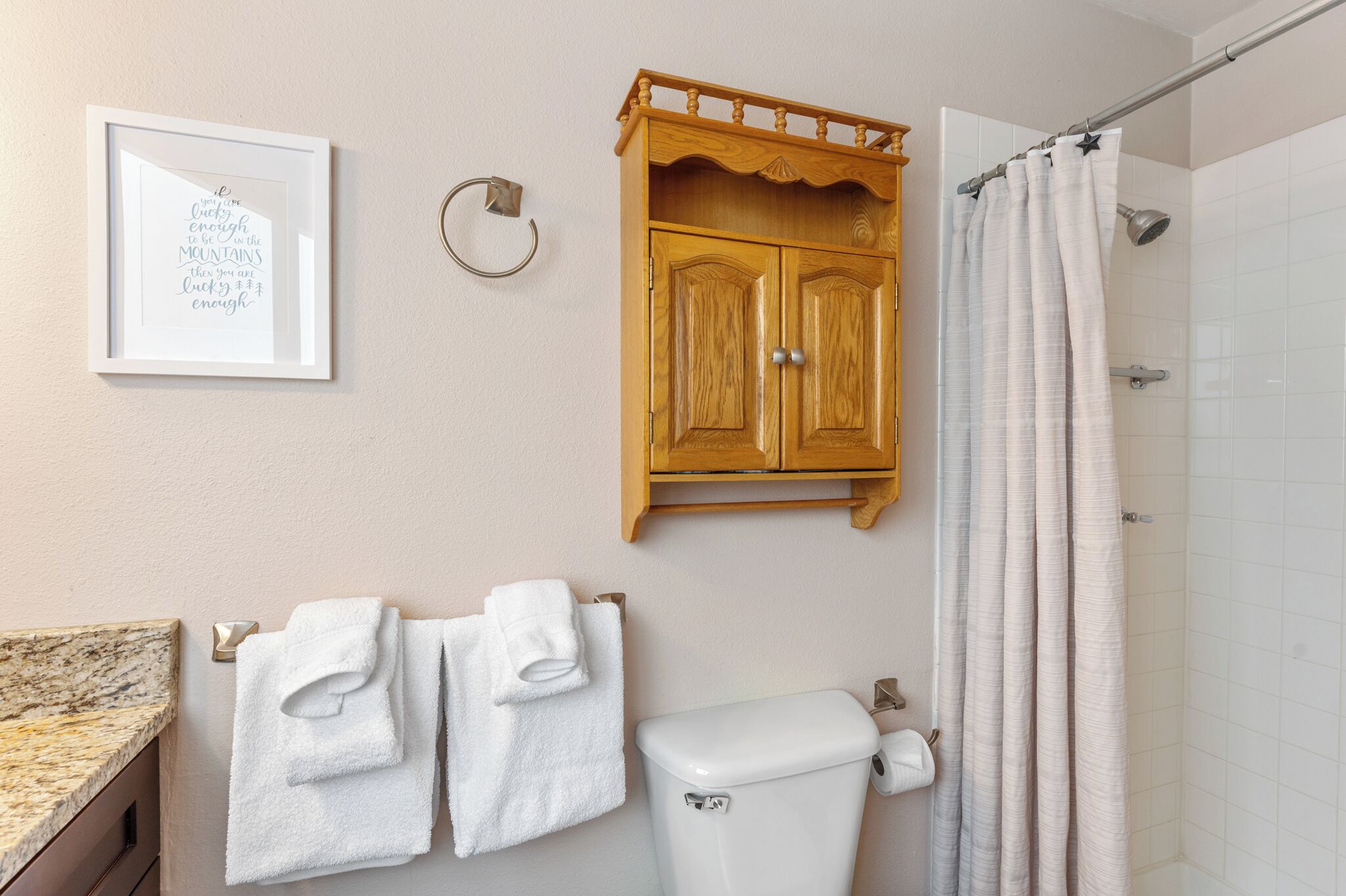 A bathroom with a toilet, a wooden cabinet, a framed inspirational quote, and a shower curtain.
