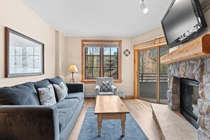 A living room with a sofa, a coffee table, a TV, a fireplace, and a window with a view of trees. - Dl8480-2 (Keystone)
