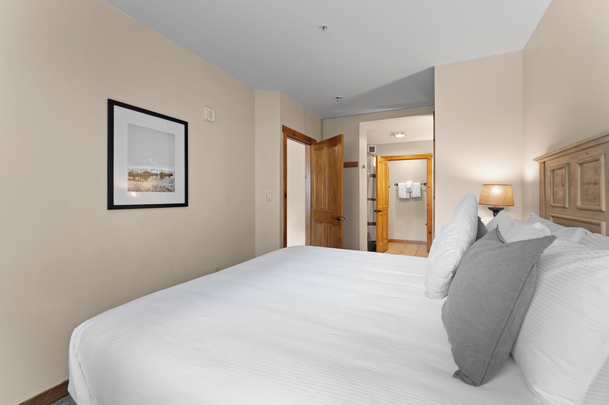 Een hotelkamer met een groot bed, een lijst met een foto aan de muur, een houten deur en een lamp.