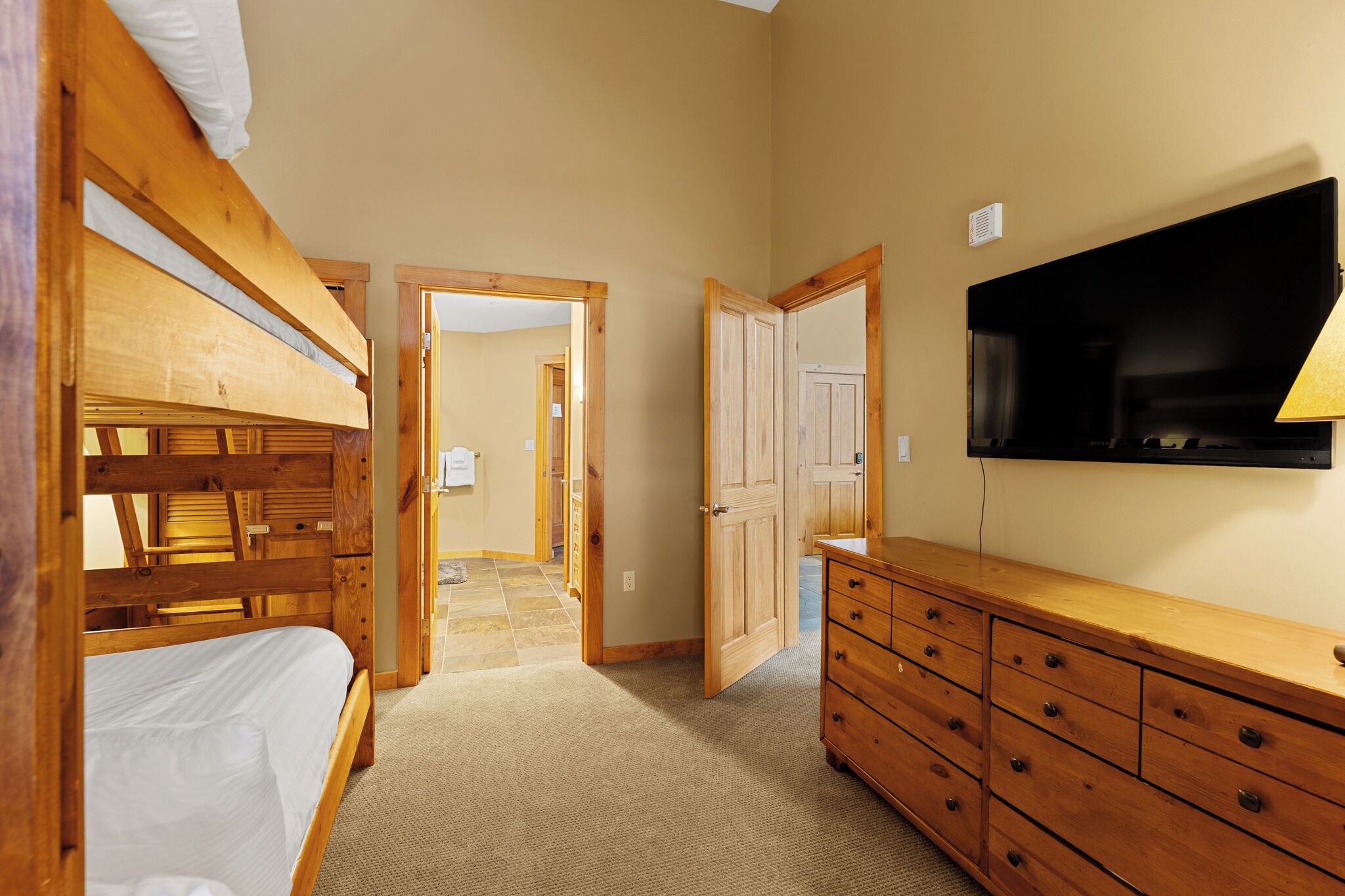 A room with bunk beds, a wooden dresser, a television, and a door leading to another room.