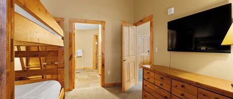 A room with bunk beds, a wooden dresser, a television, and a door leading to another room.