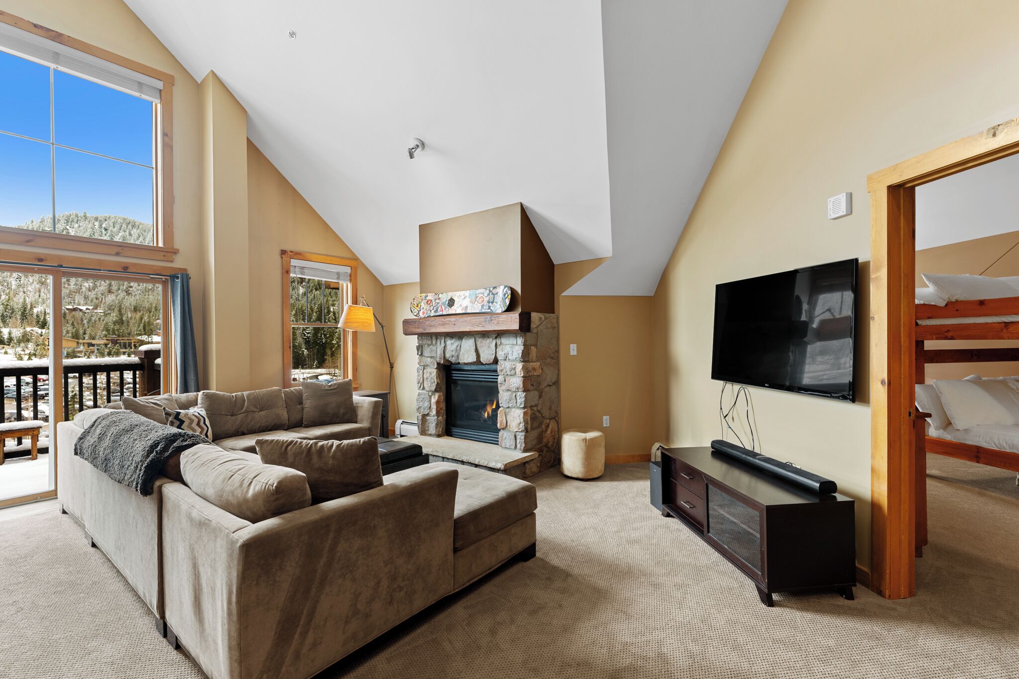 Ein geräumiges Wohnzimmer mit Kamin, einer Sofagarnitur, einem Fernseher und einem Balkon mit Blick auf eine verschneite Landschaft.