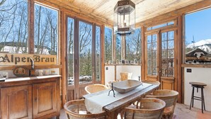 Un intérieur en bois avec une table à manger, des chaises en osier et une vue sur des montagnes enneigées.