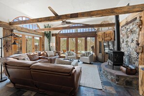 Ein geräumiges Wohnzimmer mit einer großen Ledersofa, Holzbalken, einem Kamin aus Stein und großen Fenstern.