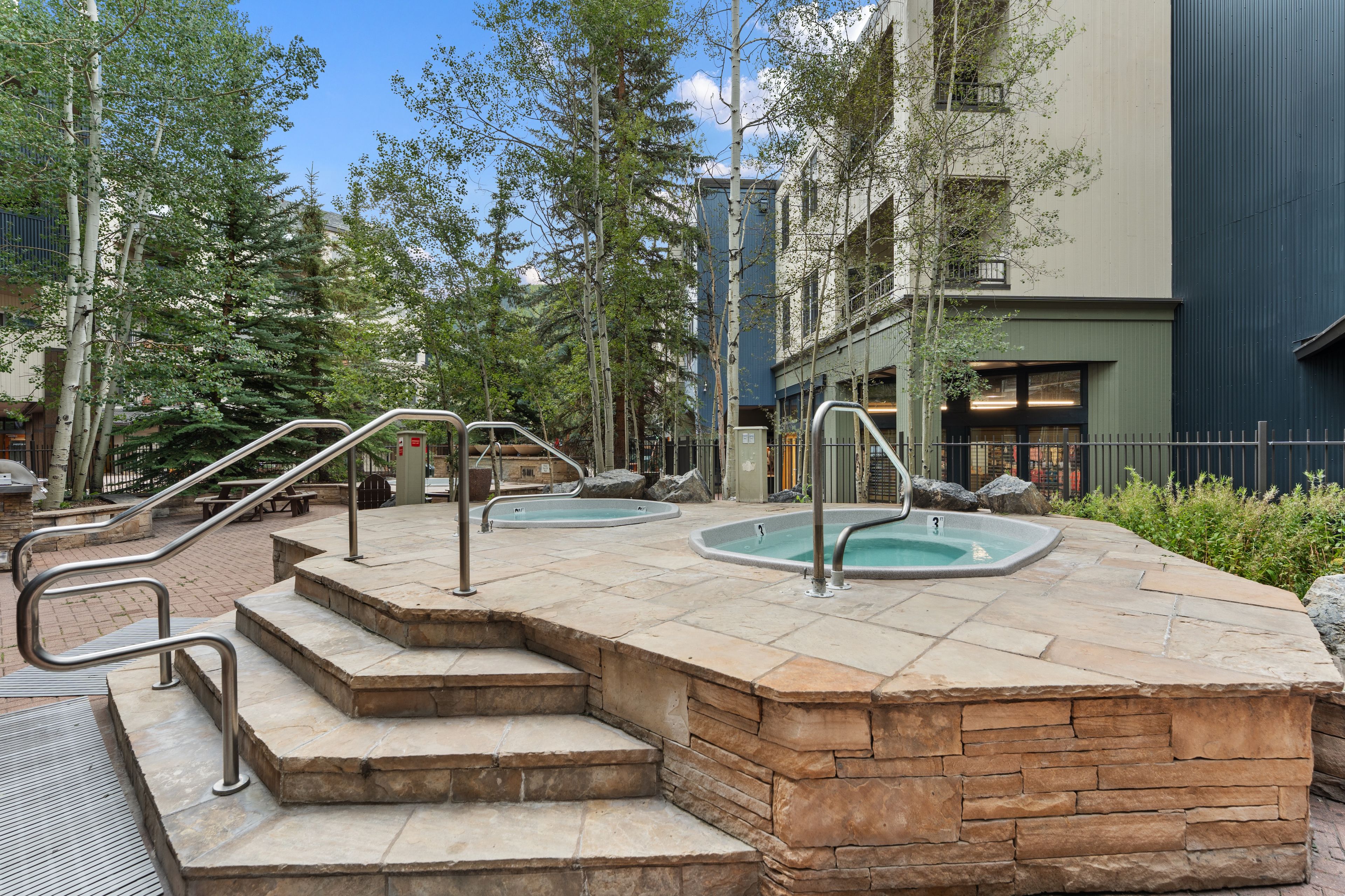 A pool area with steps leading to the pool, surrounded by trees and a building.