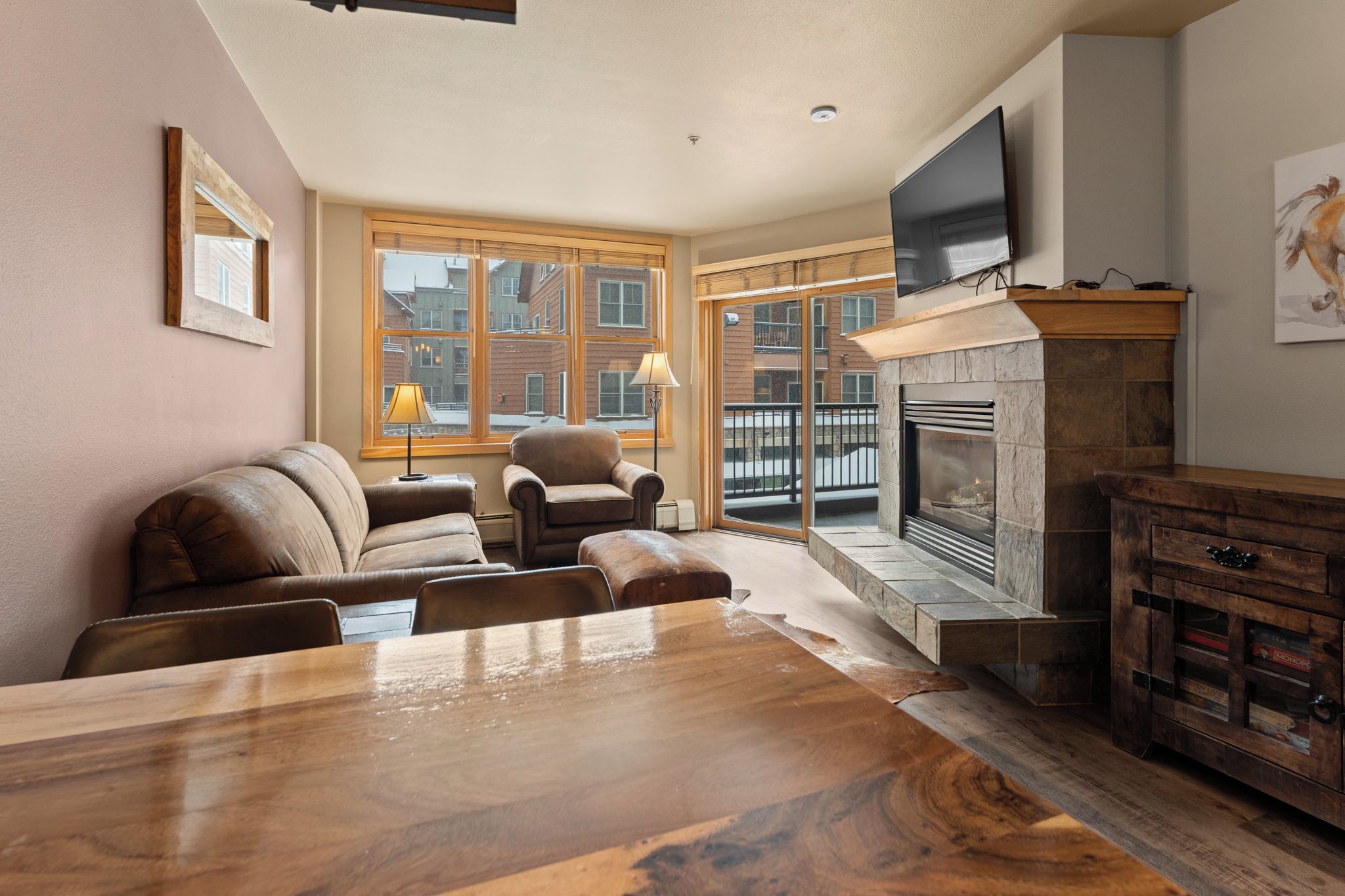 A living room with a fireplace, leather sofas, a wooden dining table, and a TV mounted on the wall.