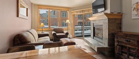 A living room with a fireplace, leather sofas, a wooden dining table, and a TV mounted on the wall.